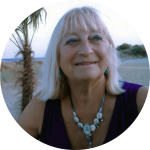 Monika Rohde | GracePoint Publishing Older woman with light hair wearing a turquoise necklace smiles at the beach.